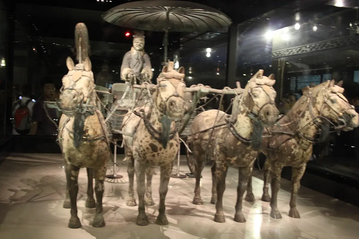 A bronze chariot with four bronze horses and a driver figure under a round canopy, in a glass display case