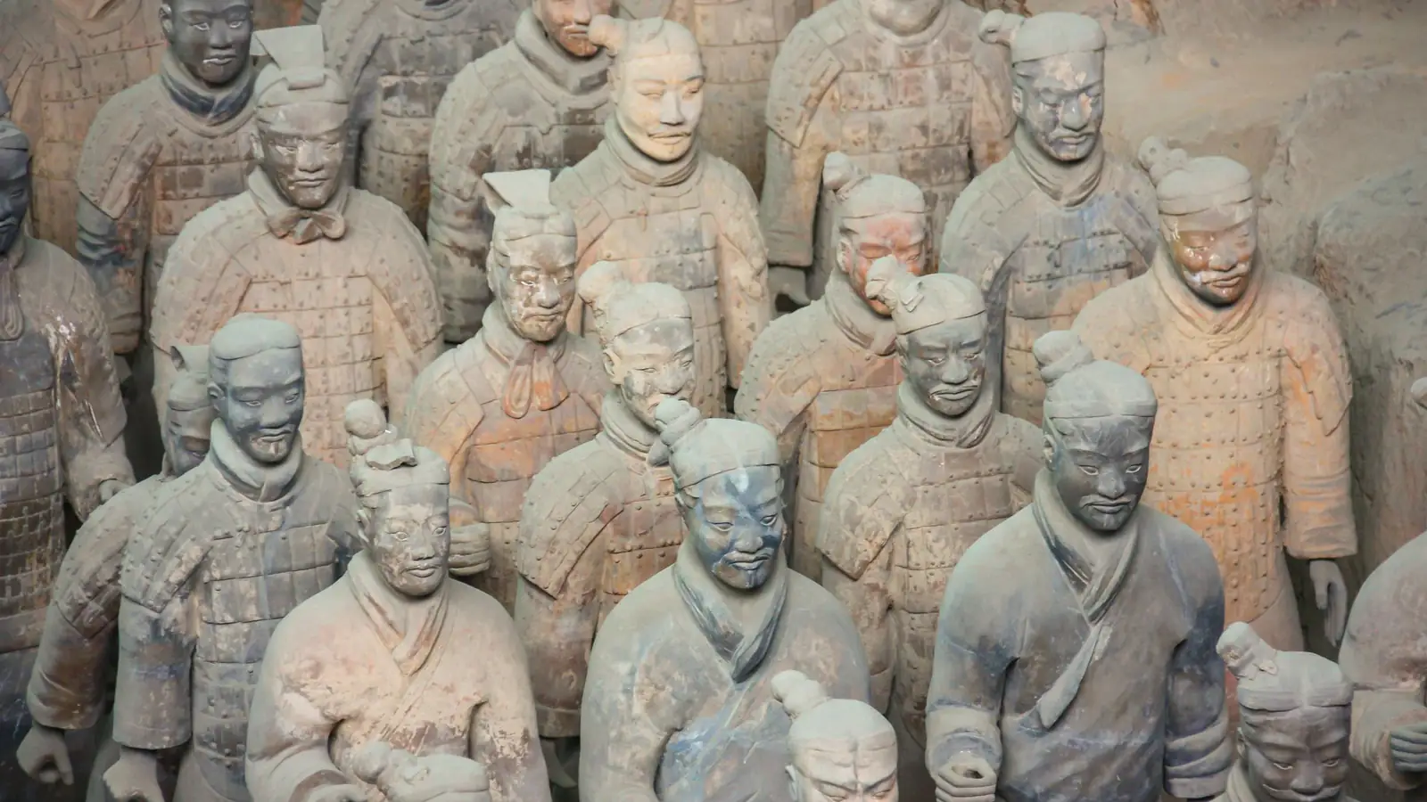 Hileras de guerreros de terracota a tamaño real en el foso de excavación, cada uno con un rostro modelado de forma individual, bañados por una cálida luz terrosa.